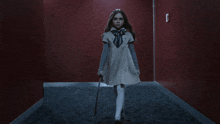 a little girl in a white dress is holding a cane in a dark hallway