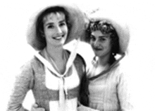 a black and white photo of two women wearing hats and dresses .