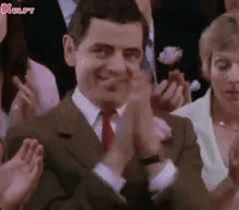 mr bean is clapping his hands in front of a crowd of people .