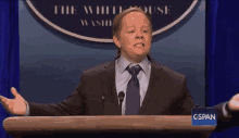 a man in a suit and tie stands at a podium in front of a sign that says " the white house "