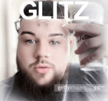 a man with a beard is holding a glass with the word glitz written on it