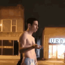 a shirtless man is standing in front of a building with the word urban on it .