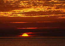 a sunset over a body of water with the sun shining through the clouds