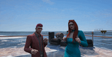 a man in a red suit and a woman in a blue dress are standing on a deck overlooking the ocean