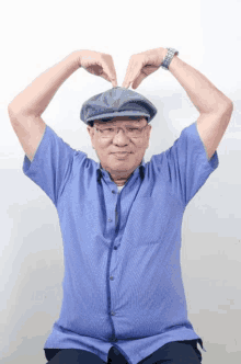 a man wearing a blue shirt and a hat is making a heart shape with his hands