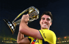 a man in a yellow polytech shirt holds a trophy in his hand