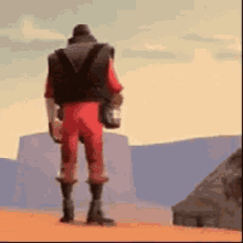 a man in a red jumpsuit is standing in the desert holding a bottle of water .