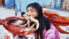 a woman in a pink jacket is eating a giant squid