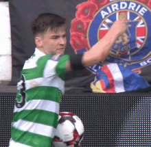 a man in a green and white striped shirt is playing soccer in front of a sign that says airdrie