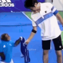 a man is giving a shirt to a child on a tennis court with an adidas logo in the background