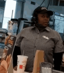 a woman wearing headphones and a hat is standing in front of a counter at a fast food restaurant .