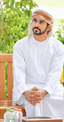 a man with a beard is sitting on a bench with his hands folded in front of him