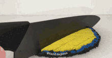 a black knife is cutting a piece of yellow and blue sand on a white surface