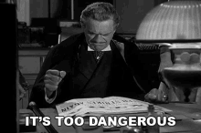 a black and white photo of a man sitting at a desk with the words it 's too dangerous written below him