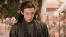 a man with long hair is wearing a black robe and standing in front of a flower arrangement .