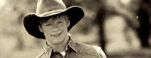 a young man wearing a cowboy hat and a denim shirt is smiling in a black and white photo .