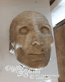 a statue of a man 's face is displayed on a white wall by digital yarns