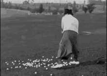 a black and white photo of a man swinging a golf club at golf balls on a golf course .