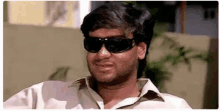 a man wearing sunglasses and a white shirt is smiling and looking at the camera .