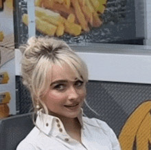 a blonde woman in a white shirt is sitting in front of a french fries sign .