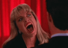 a woman is screaming at a man in front of a red curtain in a room .