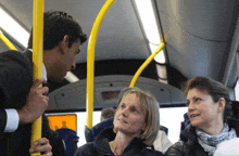 a man talking to two women on a bus with a yellow pole