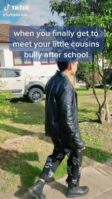 a man wearing a leather jacket and skull pants is walking down a sidewalk in front of a truck and a house