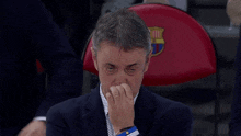 a man in a suit covering his nose in front of a chair with a fcb logo on it