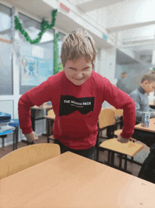 a boy wearing a red shirt that says the north face makes a funny face