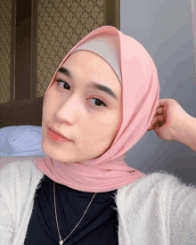 a woman wearing a pink hijab and a white sweater