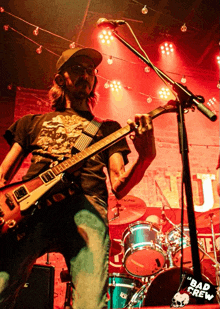 a man playing a guitar in front of a microphone with a sign that says le bad crew