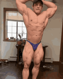 a muscular man in a blue thong is standing in front of a window