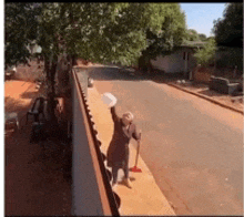 a woman standing on a sidewalk holding a broom and a bucket