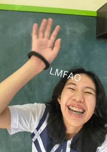 a girl with braces on her teeth holds her hand up in front of a blackboard with lmfao written on it