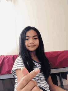 a young girl sitting on a bed making a heart with her fingers