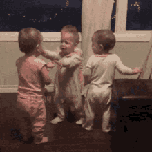 three babies are dancing in a room with a window in the background