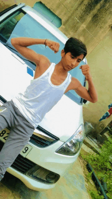 a young man flexes his muscles in front of a white car with a license plate that says 8l