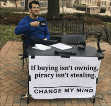 a man sits at a table with a sign that reads change my mind