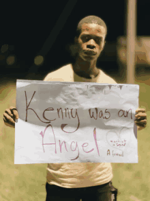 a man holds a sign that says kenny was an angel