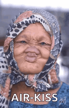 an elderly woman wearing a scarf around her head is making a funny face and says air kiss .