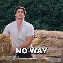 a man in a white shirt is standing in front of a pile of hay and a sign that says " no way "