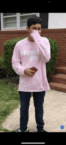 a man wearing a pink shirt that says hentai covering his face