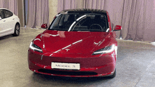 a red tesla model 3 car is parked in a garage