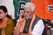 a man with a mustache is talking on a cell phone in front of a green and orange banner with the letter p on it