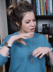 a woman wearing a blue shirt and a necklace with a key on it is sitting in front of a bookshelf