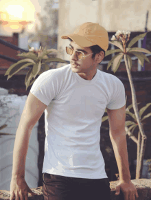 a man wearing a white t-shirt and a yellow hat is leaning against a wall