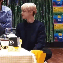 a young man is sitting at a table with a cup of coffee and a box of butter .