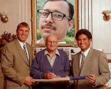 three men are standing in front of a framed picture of a man with glasses