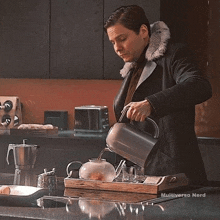 a man is pouring water into a teapot on a tray on a kitchen counter .