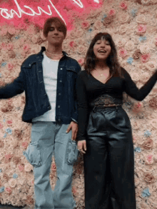 a man and a woman are posing in front of a wall of flowers with the word baby on it